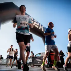 Des coureurs franchissent une arche de départ, prêts à se préparer pour le semi-marathon. Le soleil brille sur la course.