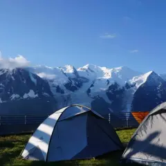 Deux tentes de bivouac aiguilles rouges face à des montagnes enneigées sous un ciel bleu.