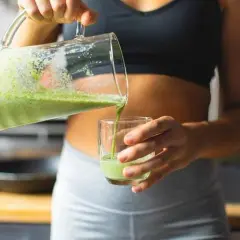 Une femme verse un smoothie vert dans un verre, un geste essentiel pour réussir son challenge 75 Hard.