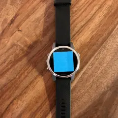 Montre connectée Garmin avec un post-it bleu sur l'écran, prête pour une aventure avec son GPS Galileo.