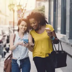 Deux amies marchent en ville, l'une montre son téléphone, l'autre mange une glace. Elles atteignent sûrement leurs 10000 pas par jour !