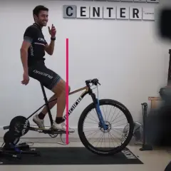 Un cycliste ajuste le recul de selle de son vélo sur un home trainer. Une ligne rose indique la mesure.