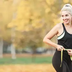 Femme souriante mesurant sa taille avec un mètre ruban, prouvant que courir fait il maigrir.