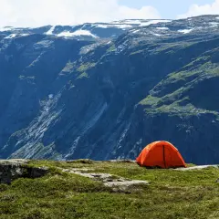 Orange tente sur un plateau rocheux, avec une vue imprenable sur des montagnes escarpées. Un endroit parfait pour un bivouac autorisé.