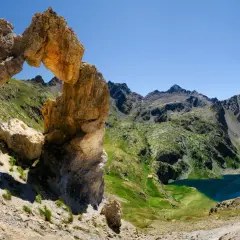 Un arc rocheux spectaculaire domine un paysage de montagne verdoyant avec des lacs bleus, une vue typique du tour du Mercantour.