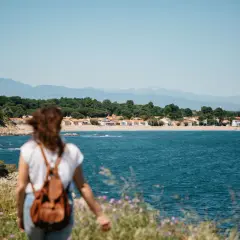 Vue sur la mer et des maisons colorées, une femme avec un sac à dos profite d'une belle randonnée.