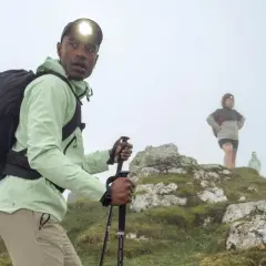 Randonneur ajustant le réglage de ses bâtons de marche sur un sentier brumeux. D'autres randonneurs sont visibles en arrière-plan.