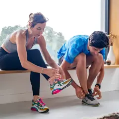 Un couple se prépare pour reprendre le sport, enfilant leurs chaussures de course près d'une fenêtre lumineuse.