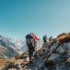 Randonneurs sur un sentier rocheux, le Tour du Mont Blanc difficulté est palpable. Paysage alpin grandiose sous un ciel bleu.