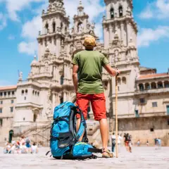 Pèlerin du **marche saint jacques de compostelle** contemplant la cathédrale. Sac à dos bleu et bâton de marche à ses côtés.