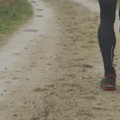 Jambes d'un coureur sur un chemin de terre, concentré sur sa cadence course à pied. Les chaussures rouges et noires s'enfoncent dans le sol humide.