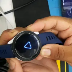 Montre Garmin avec un triangle bleu lumineux sur l'écran. La montre est tenue par des mains.