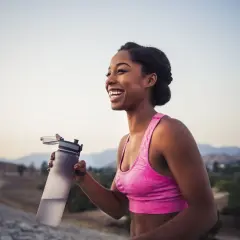 Une femme souriante tient une bouteille d'eau après son entraînement. Le sport est essentiel pour la perte de poids et le bien-être.