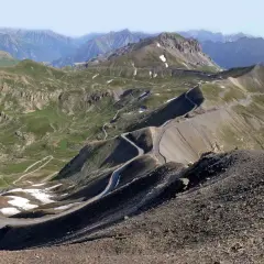 Vue panoramique du col de la Bonette, avec sa route sinueuse traversant des paysages montagneux verdoyants et rocailleux.