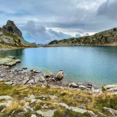 Lac de montagne aux eaux bleues, entouré de rochers et d'herbes sèches. Un paysage sauvage, peut-être une randonnée de gr 52 difficulté.