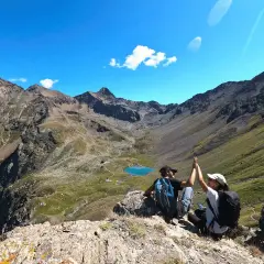 Deux randonneurs célèbrent leur succès au sommet, avec un lac bleu et des montagnes majestueuses en arrière-plan. Une parfaite randonnée à Aoste.