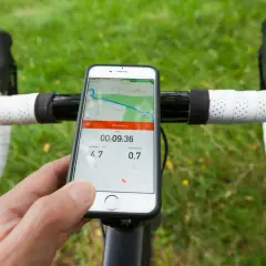 Un cycliste utilise son smartphone avec une application type komoot ou Strava pour suivre sa sortie. La carte et les stats sont visibles.