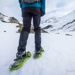 Une personne en tenue d'hiver est prête à marcher avec des raquettes dans un paysage enneigé et montagneux.