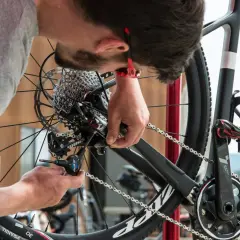 Un mécanicien ajuste le **réglage du dérailleur arrière** d'un vélo de course avec un outil Allen.