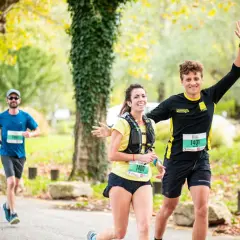 Coureurs souriants lors d'une course, un homme agite la main. Idéal pour un plan entraînement semi-marathon débutant.