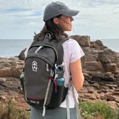Jeune femme avec un sac à dos, prête à faire de la randonnée sur un sentier côtier rocheux, face à la mer.