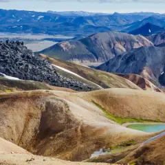 Randonneuse solitaire explorant les paysages colorés et volcaniques du trek Landmannalaugar, avec des montagnes aux teintes ocre, vertes et bleues.