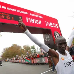 Eliud Kipchoge franchit la ligne d'arrivée, record marathon homme officiellement battu. Il brandit le drapeau kenyan, célébrant son exploit.