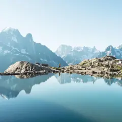 Un lac alpin reflète des montagnes majestueuses. Une randonneuse admire le paysage, un aperçu des meilleures randonnées en France.