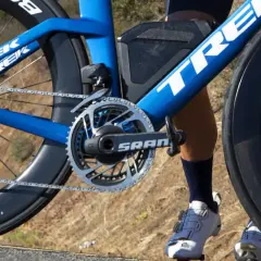 Démonter pédale vélo : gros plan sur le pédalier SRAM d'un vélo de course Trek bleu, avec une jambe de cycliste en chaussures blanches.