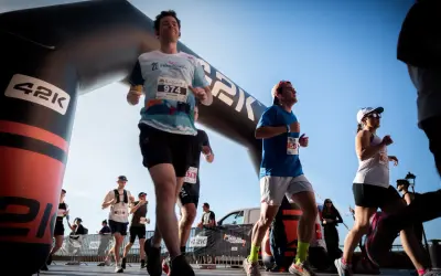 Des coureurs franchissent une arche de départ, prêts à se préparer pour le semi-marathon. Le soleil brille sur la course.