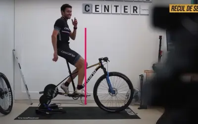 Un cycliste ajuste le recul de selle de son vélo sur un home trainer. Une ligne rose indique la mesure.