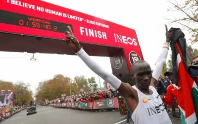 Eliud Kipchoge franchit la ligne d'arrivée, record marathon homme officiellement battu. Il brandit le drapeau kenyan, célébrant son exploit.