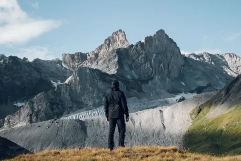 Un randonneur contemple les sommets majestueux du tour des glaciers de la Vanoise 3 jours. Paysage alpin grandiose.