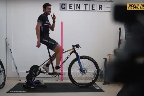 Un cycliste ajuste le recul de selle de son vélo sur un home trainer. Une ligne rose indique la mesure.