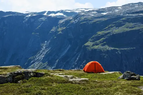 Orange tente sur un plateau rocheux, avec une vue imprenable sur des montagnes escarpées. Un endroit parfait pour un bivouac autorisé.