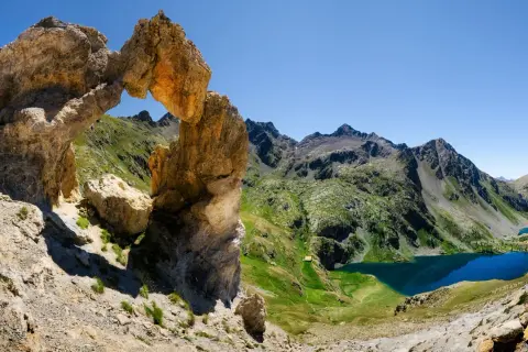 Un arc rocheux spectaculaire domine un paysage de montagne verdoyant avec des lacs bleus, une vue typique du tour du Mercantour.