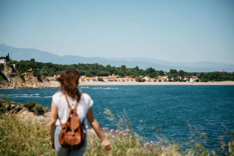 Vue sur la mer et des maisons colorées, une femme avec un sac à dos profite d'une belle randonnée.
