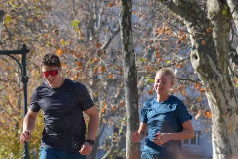 Un homme et une femme souriants courent dans un parc en automne, profitant de leur endurance fondamentale.