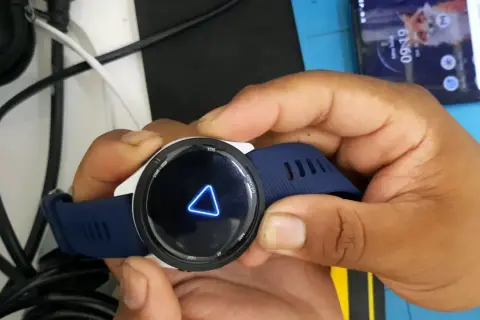 Montre Garmin avec un triangle bleu lumineux sur l'écran. La montre est tenue par des mains.