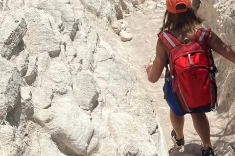 Randonneuse avec sac à dos rouge sur un sentier rocailleux, tout l'équipement nécessaire pour le GR20.