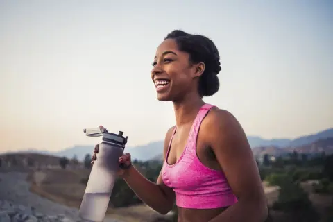 Une femme souriante tient une bouteille d'eau après son entraînement. Le sport est essentiel pour la perte de poids et le bien-être.