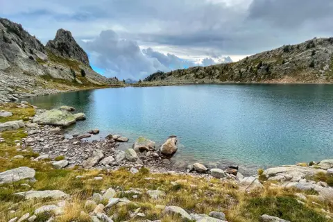 Lac de montagne aux eaux bleues, entouré de rochers et d'herbes sèches. Un paysage sauvage, peut-être une randonnée de gr 52 difficulté.