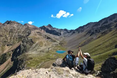 Deux randonneurs célèbrent leur succès au sommet, avec un lac bleu et des montagnes majestueuses en arrière-plan. Une parfaite randonnée à Aoste.