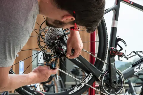 Un mécanicien ajuste le **réglage du dérailleur arrière** d'un vélo de course avec un outil Allen.