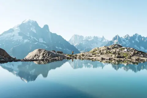 Un lac alpin reflète des montagnes majestueuses. Une randonneuse admire le paysage, un aperçu des meilleures randonnées en France.
