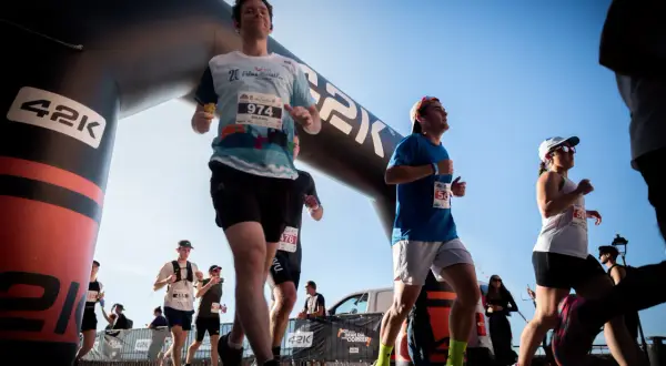 Des coureurs franchissent une arche de départ, prêts à se préparer pour le semi-marathon. Le soleil brille sur la course.