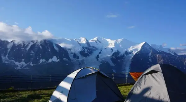 Deux tentes de bivouac aiguilles rouges face à des montagnes enneigées sous un ciel bleu.