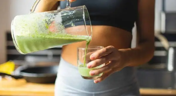 Une femme verse un smoothie vert dans un verre, un geste essentiel pour réussir son challenge 75 Hard.