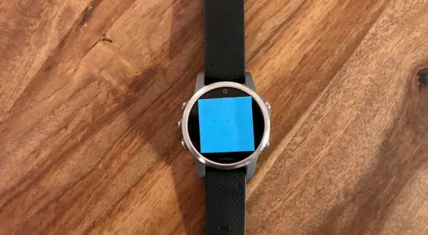 Montre connectée Garmin avec un post-it bleu sur l'écran, prête pour une aventure avec son GPS Galileo.
