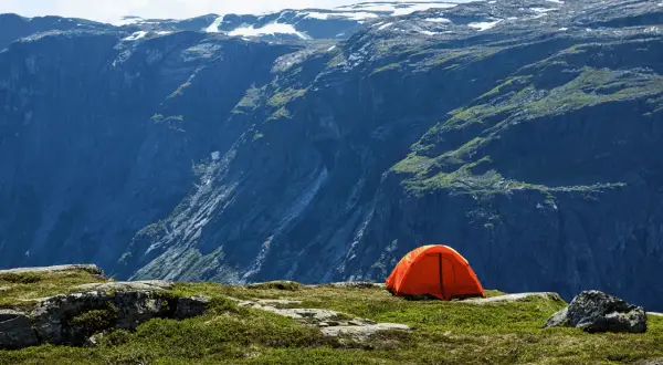 Orange tente sur un plateau rocheux, avec une vue imprenable sur des montagnes escarpées. Un endroit parfait pour un bivouac autorisé.